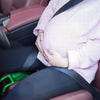 Person sitting in a car with hands on a green object, wearing a pink sweater.