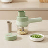 A light green manual food chopper with a clear container filled with chopped garlic, shown on a beige countertop with its lid, a small accessory cup, and a white bowl of green beans.